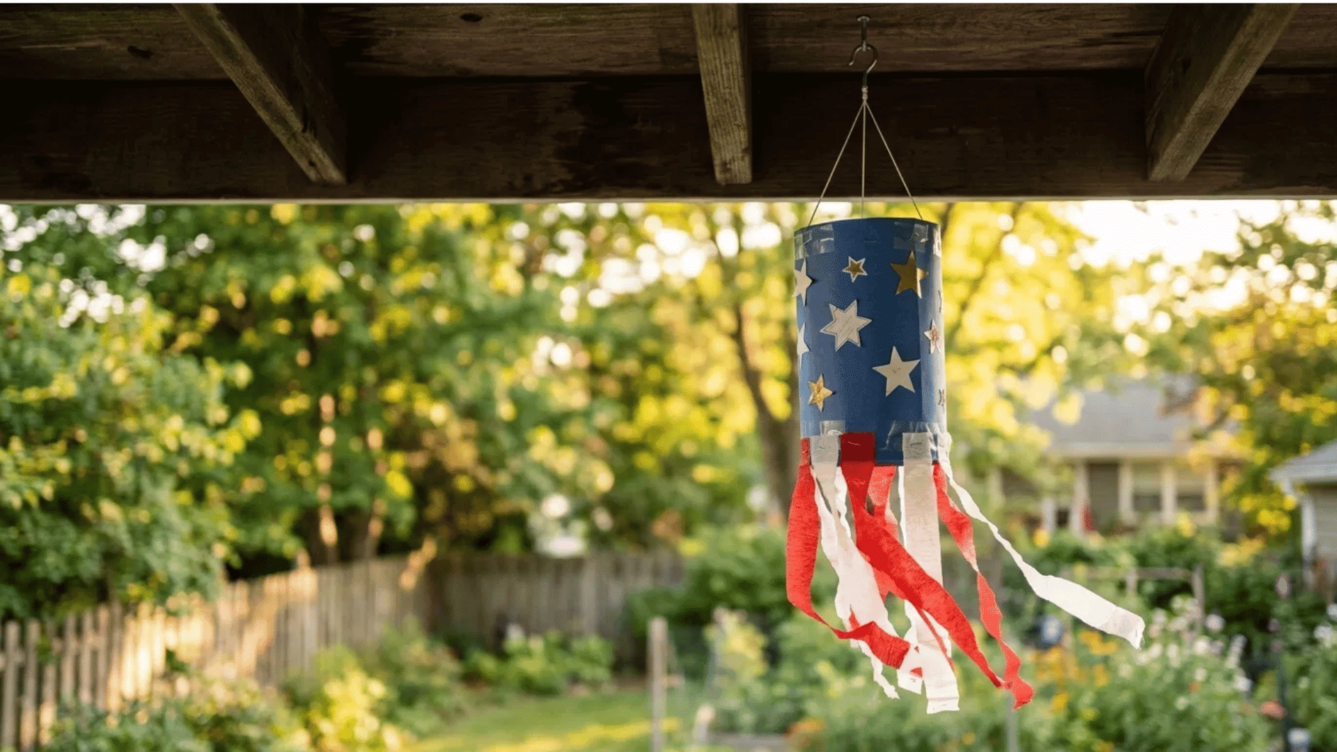 patriotic windsock with red and white streamers hanging from a porch beam at sunset