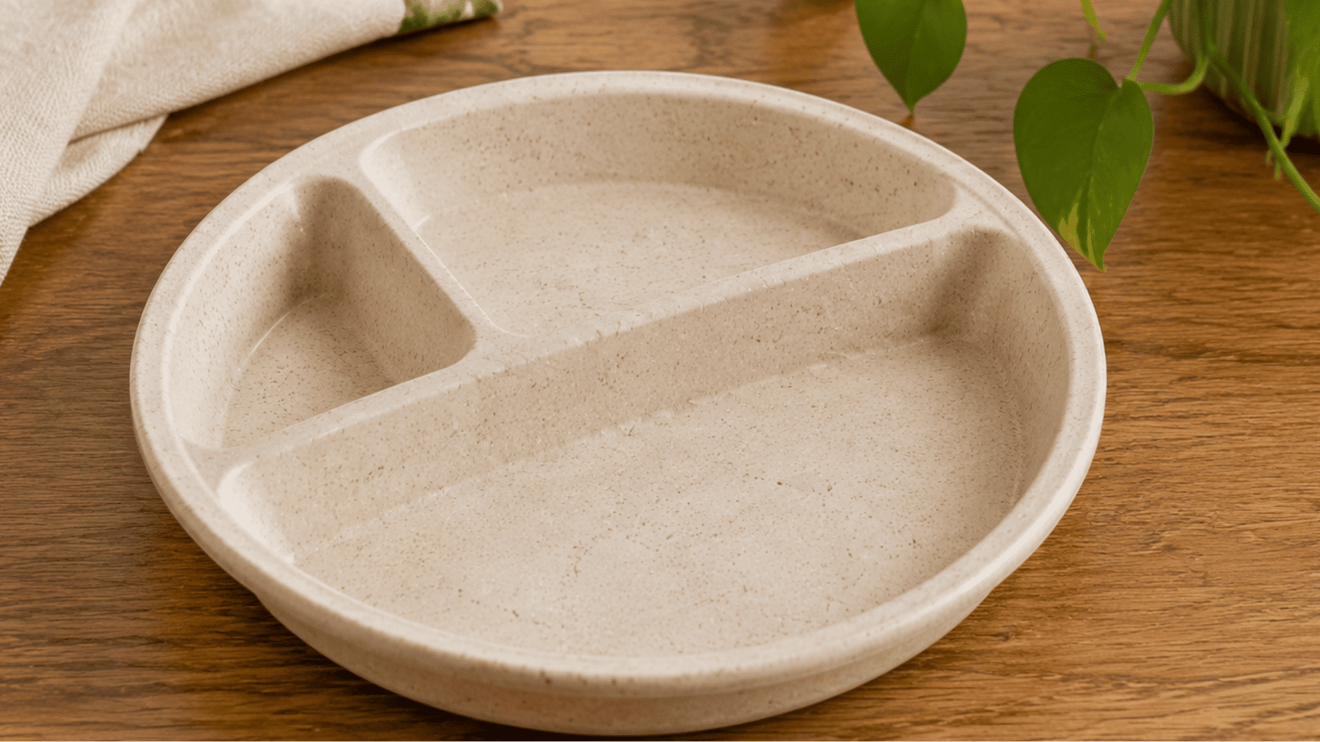 **Alt Text:** plant based kids plate with natural fiber texture and divided sections placed on a wooden table with green plants nearby