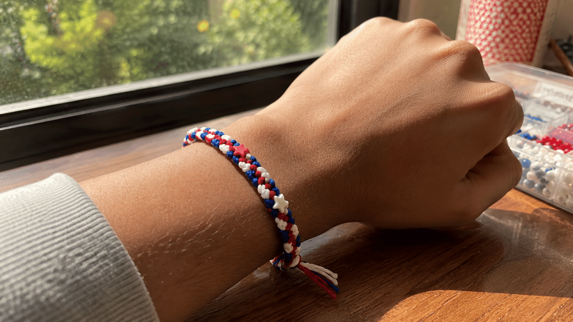 red white and blue star bead friendship bracelet worn on a wrist near a window