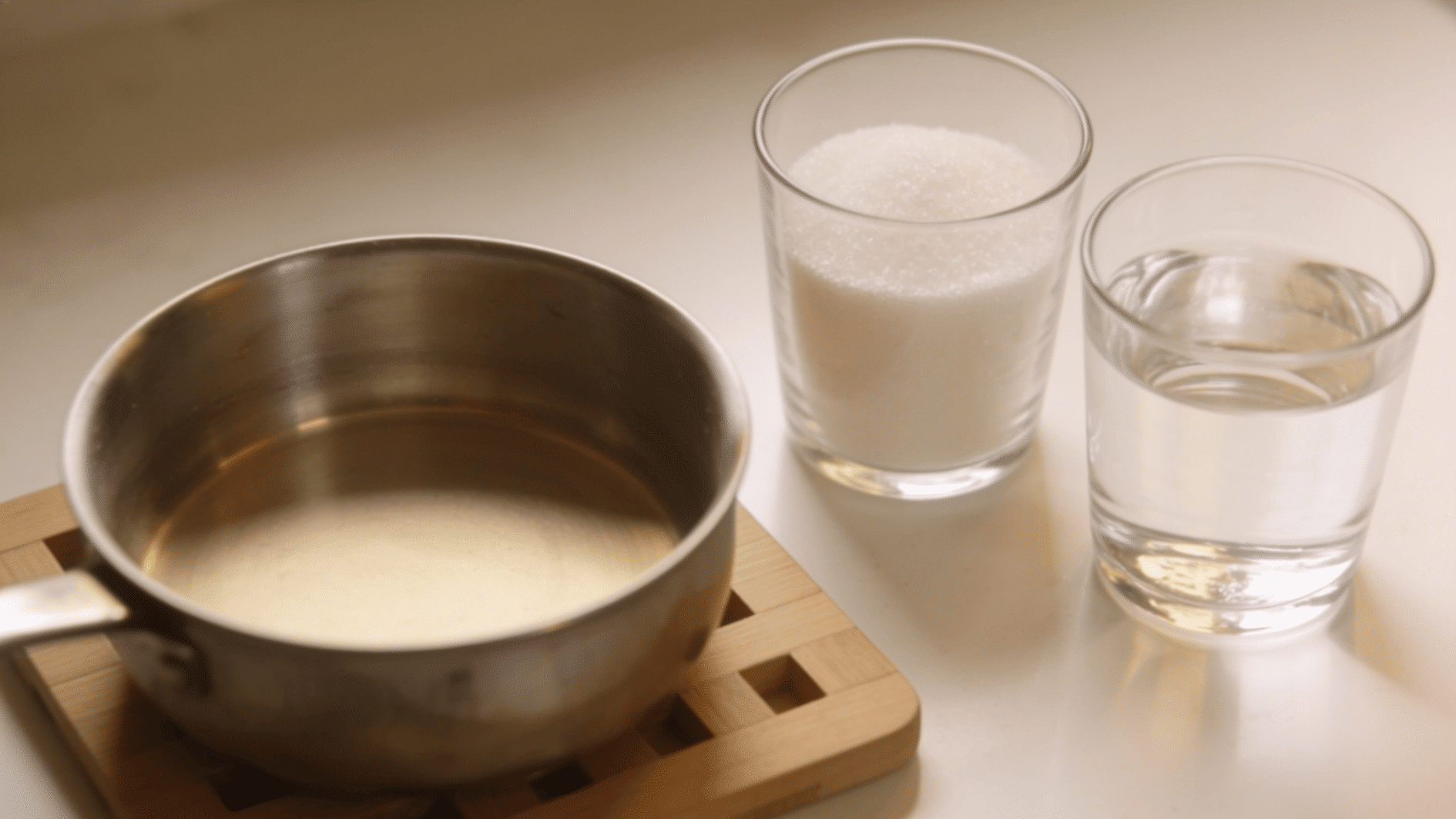 saucepan beside equal glasses of sugar and water prepared for making simple syrup on the sunny kitchen counter (1)