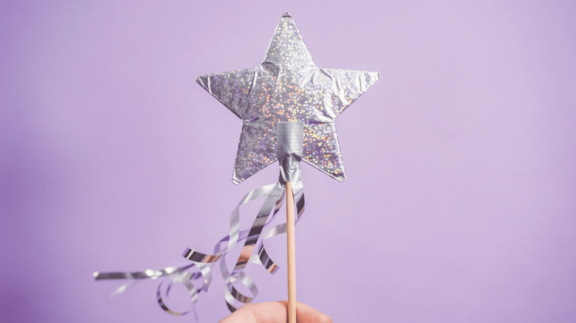 sparkly foil-covered star craft taped to a wooden craft stick with ribbon streamers hanging below, held up against a soft purple background