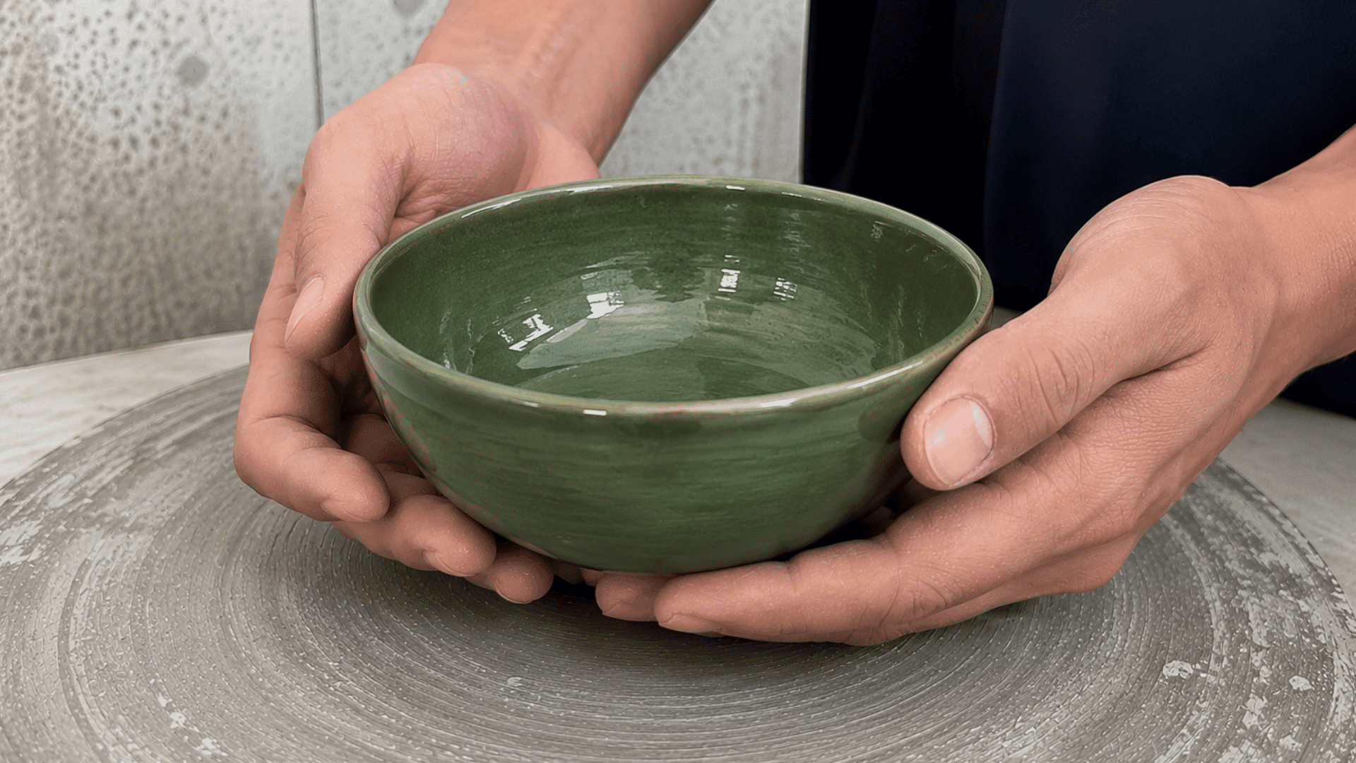 Two hands holding a finished glossy green glazed ceramic bowl, complete after its final kiln firing.