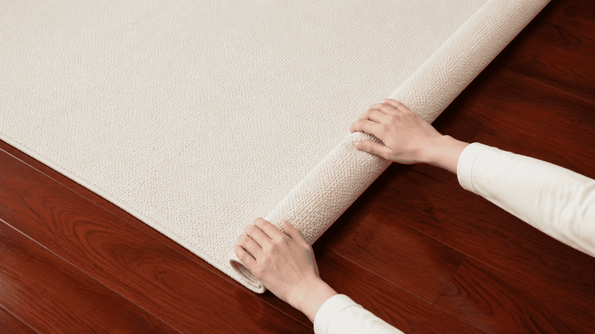 close up scene showing a cream rug being lifted over a redwood floor in a natural home setting