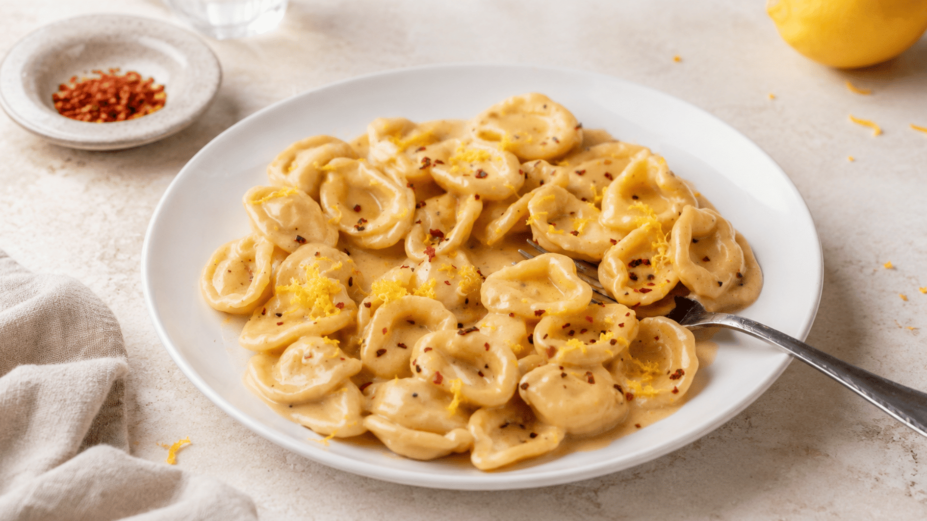 creamy lemon pasta topped with red pepper flakes and fresh lemon zest served on a white plate with fork