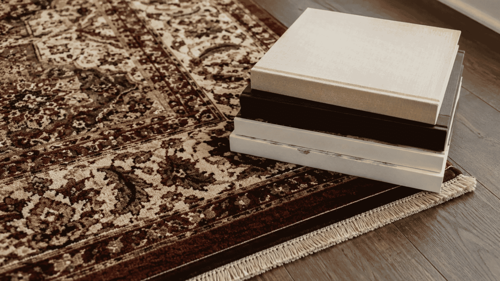 stacked books holding down a curled area rug corner on a wooden floor in a warm natural living room setting