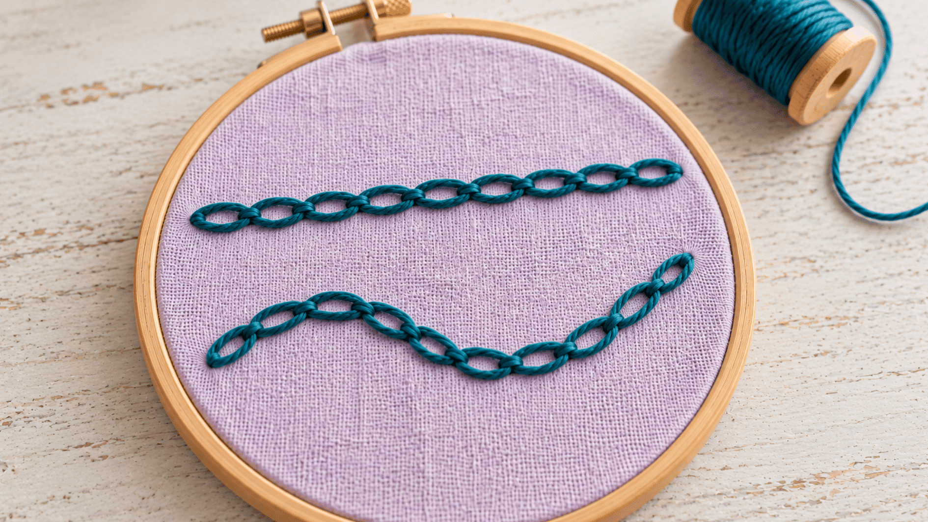 teal chain stitch embroidery on lilac linen showing large linked oval loops in two clear rows