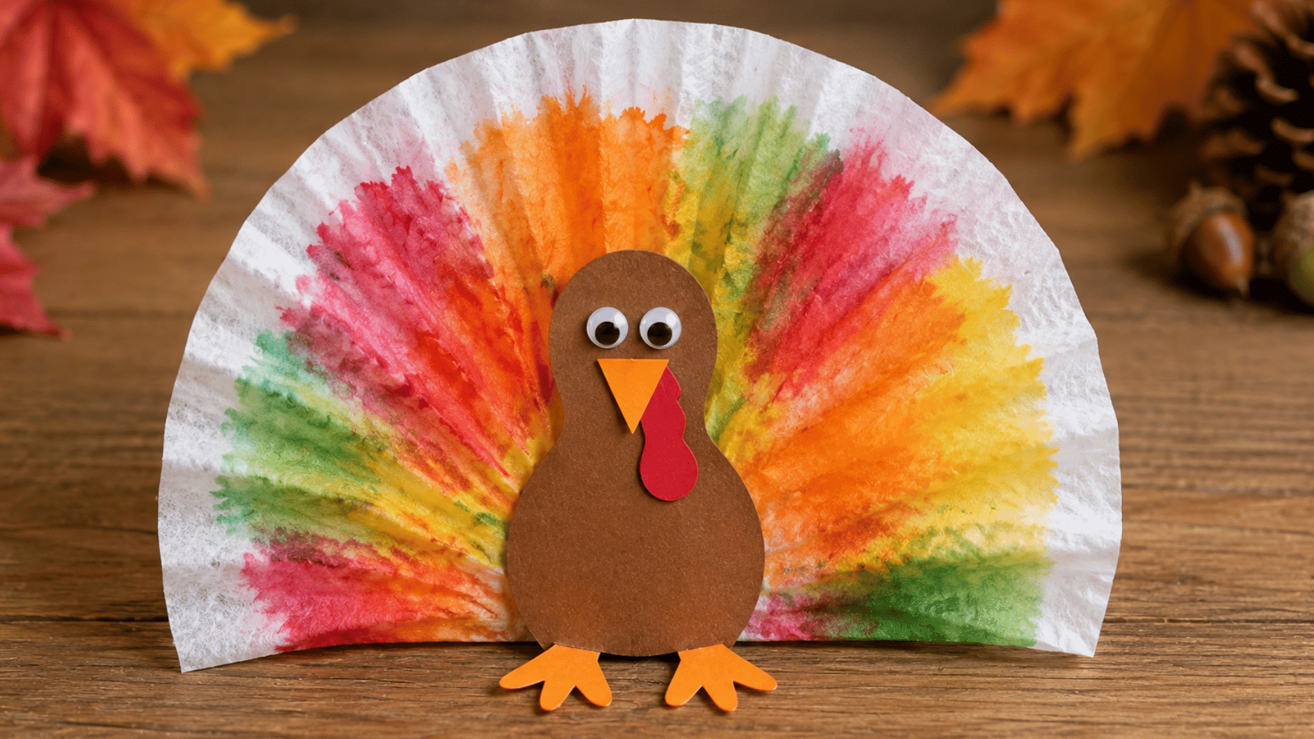 coffee filter turkey craft with blended colorful tail feathers and a brown paper body on a wooden table