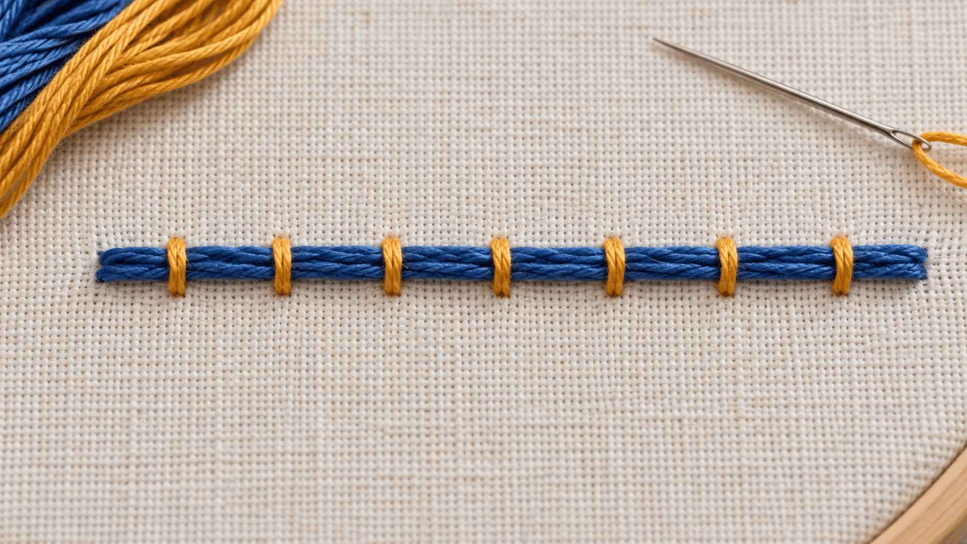 blue couching stitch secured with evenly spaced golden stitches on cream embroidery fabric