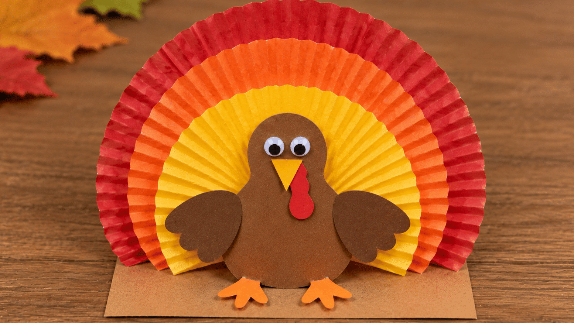 cupcake liner turkey craft with layered colorful feathers, brown paper body, beak, wattle, and feet