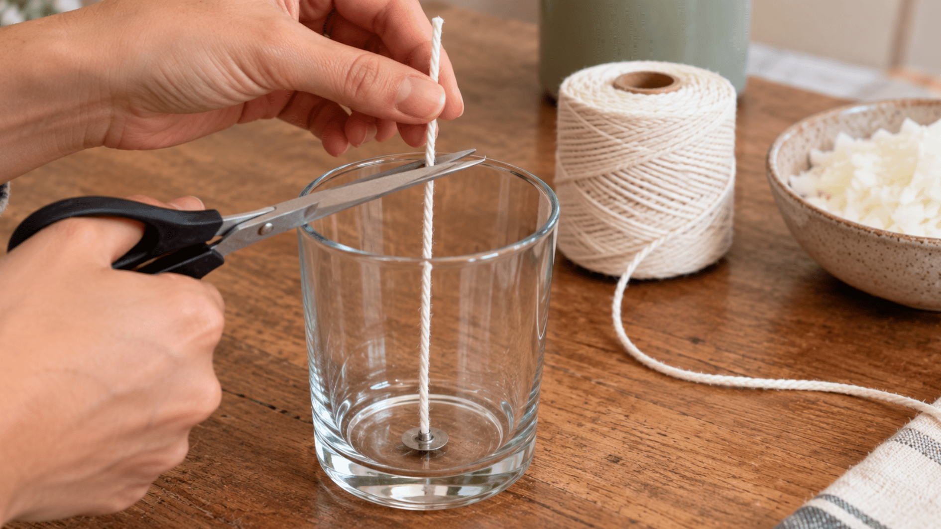 hands cutting cotton string slightly longer than a glass candle jar before making a homemade wick