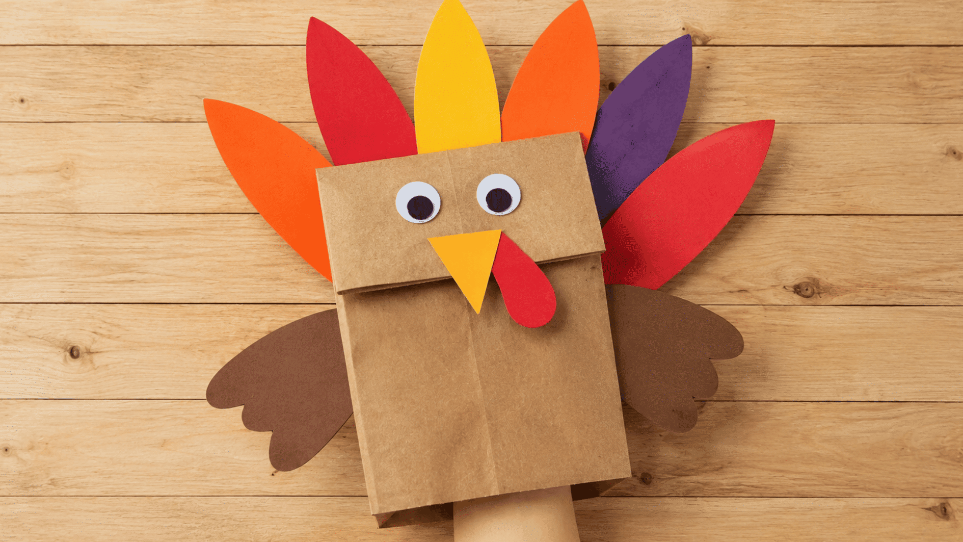 brown paper bag turkey puppet with colorful feathers, paper wings, beak, wattle, and googly eyes