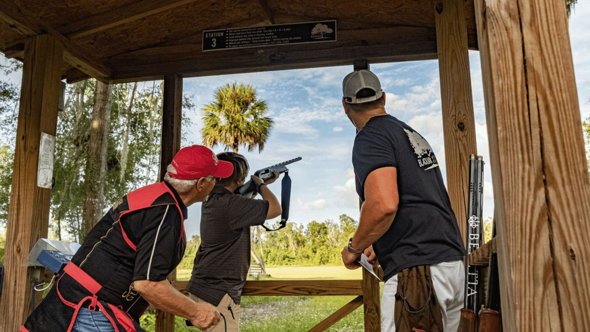 people practicing clay shooting at an outdoor range with wooden shooting station and green field background