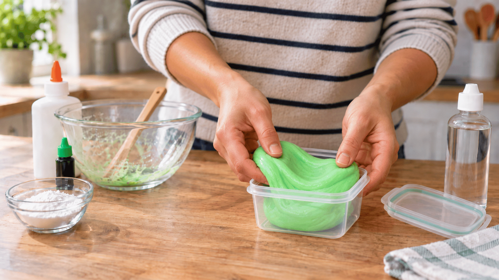 finished green homemade slime being stretched beside an open airtight container ready for storage