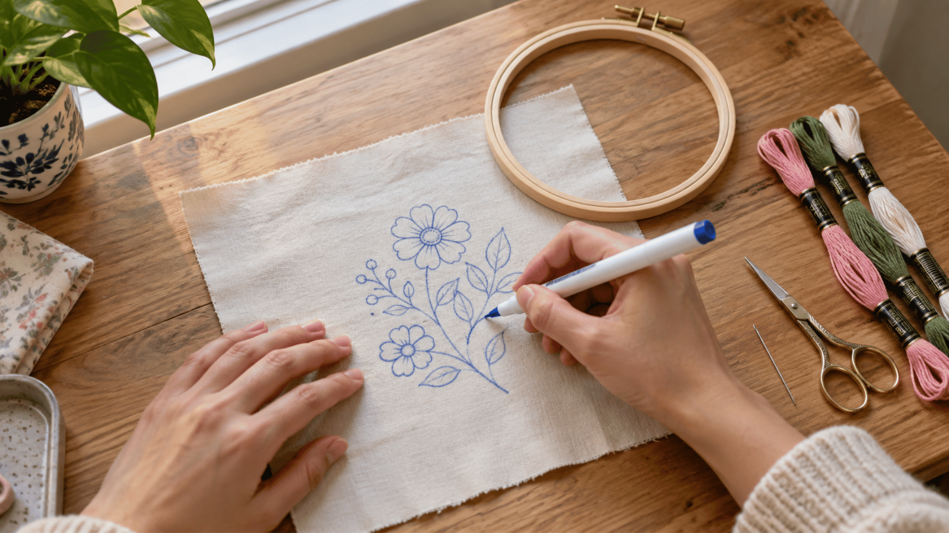 adult hands transferring a simple floral embroidery design onto cotton fabric before placing it in a wooden hoop